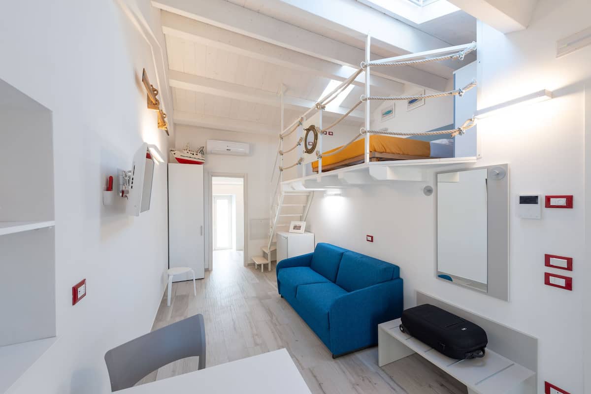 Une petite pièce avec des lits superposés, un canapé bleu, une petite table et une valise.