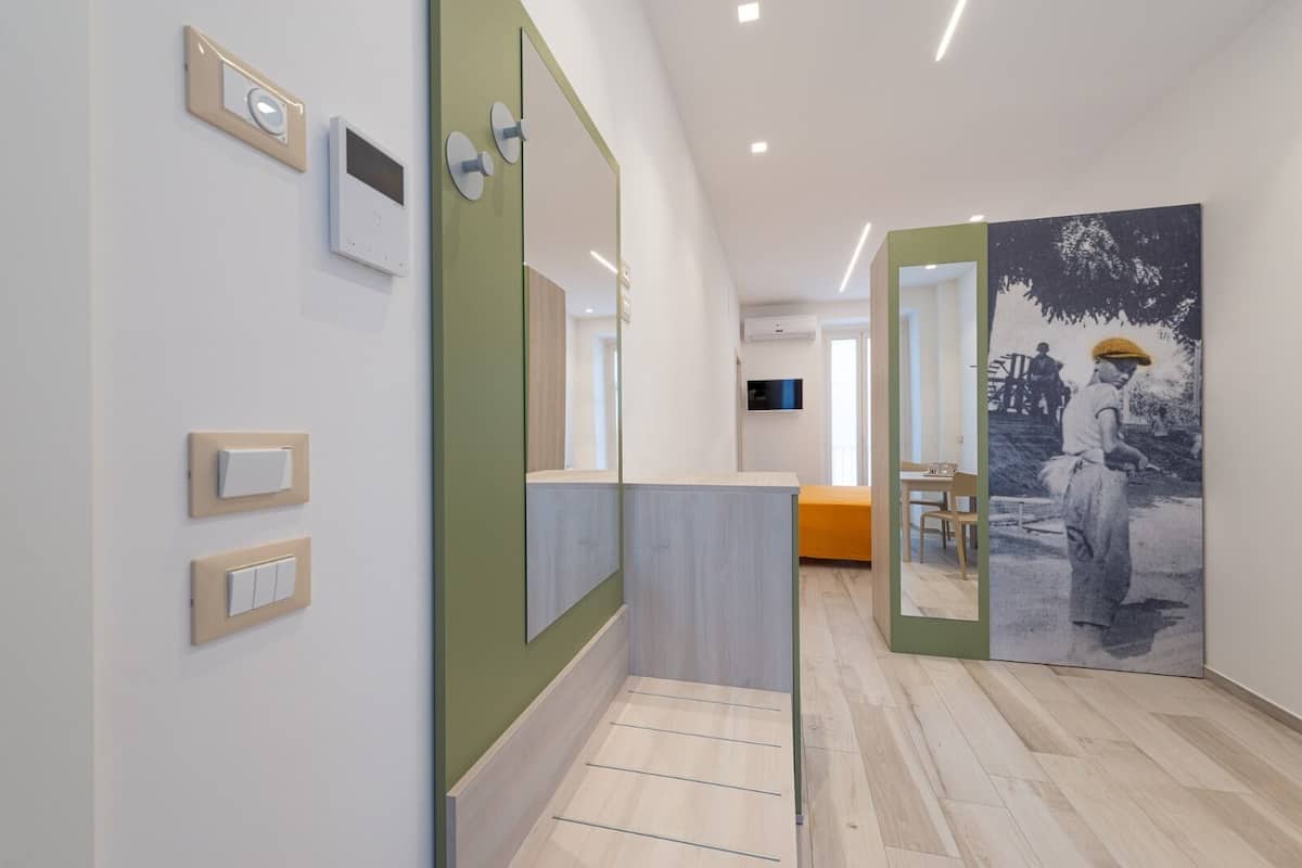 Une chambre d’hôtel moderne avec un plancher en bois, un bureau avec une chaise, un lit recouvert d’une couverture orange et un grand miroir.