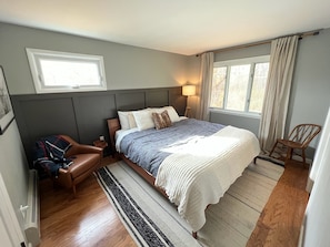 A bedroom with a bed, a chair, a small table, and a window.