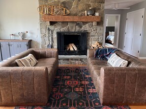 A cozy living room with a stone fireplace, leather sofas, and a patterned rug.