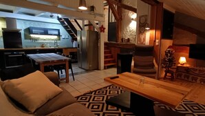 Ein gemütlicher Wohnbereich mit Couch, Holz-Couchtisch und einem gemusterten Teppich. Im Hintergrund ist eine Küche mit modernen Geräten und einem Essbereich erkennbar.
