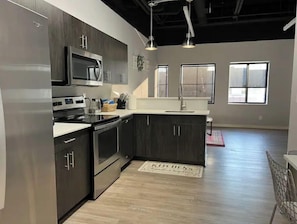 A modern kitchen with dark cabinetry, stainless steel appliances, and a large window providing natural light.