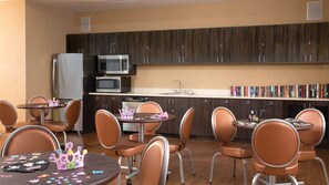 A modern kitchen with dark wood cabinets, stainless steel appliances, and a dining area with orange chairs and a small table.