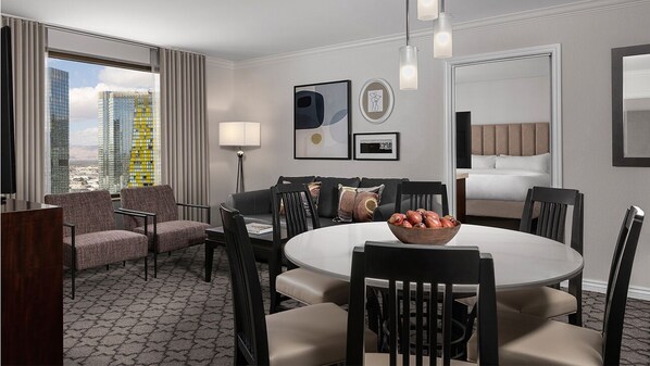 A hotel room with a dining area, a sofa, a bed, and a city view.