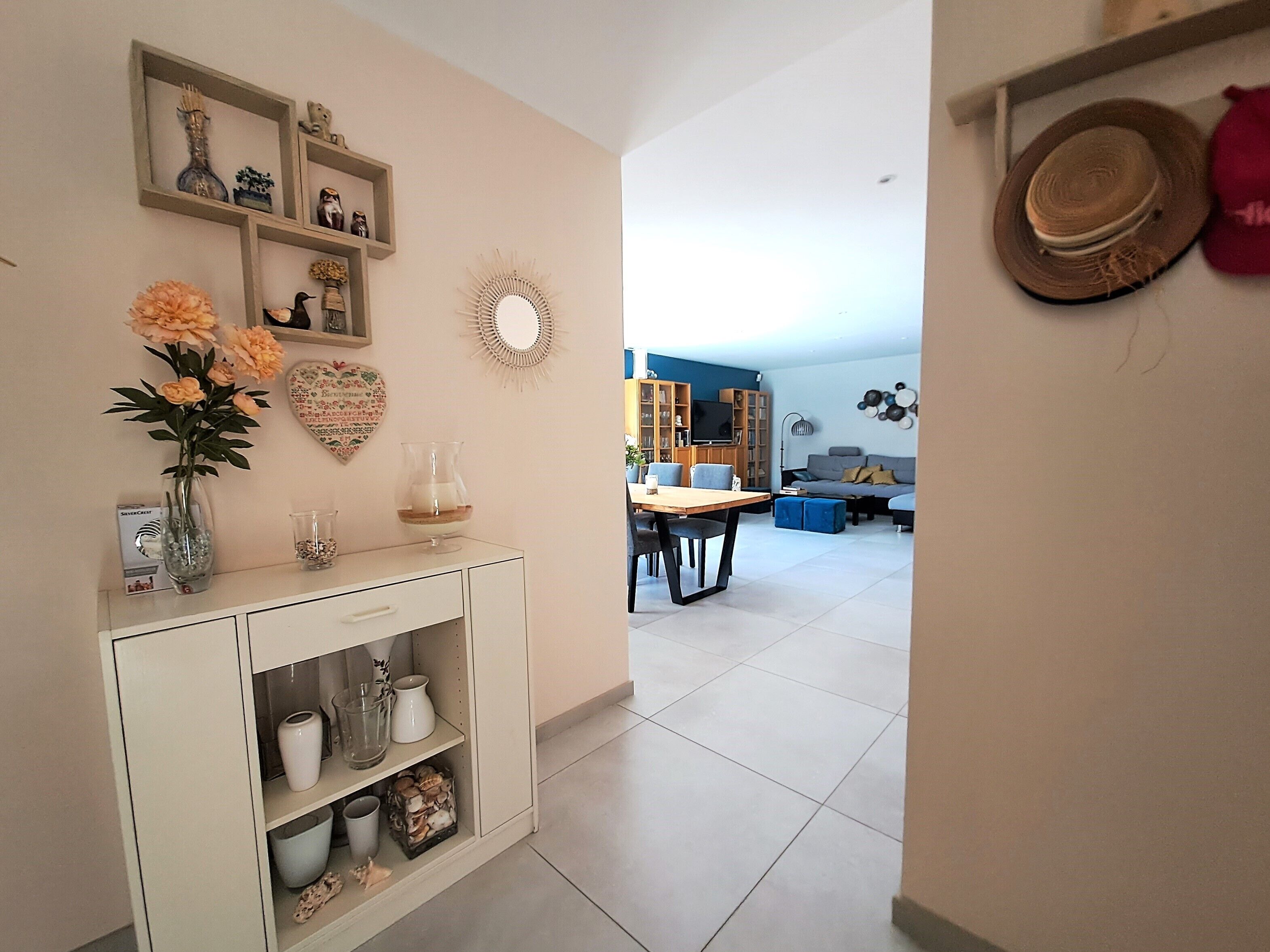 A living room with a dining area, featuring a white console table with decorative items, a sofa, and a television.