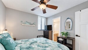 A bedroom with a bed, a ceiling fan, a dresser, a TV, and a door. - Gulf-Front Condo | Private Balcony, 3 Pools (1 Heated) (Panama City Beach)
