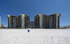 A beachfront hotel with multiple floors and balconies, a sandy foreground, and a clear blue sky. - Gulf-Front Condo, Balcony, 3 Pools, 1 Heated (Panama City Beach)