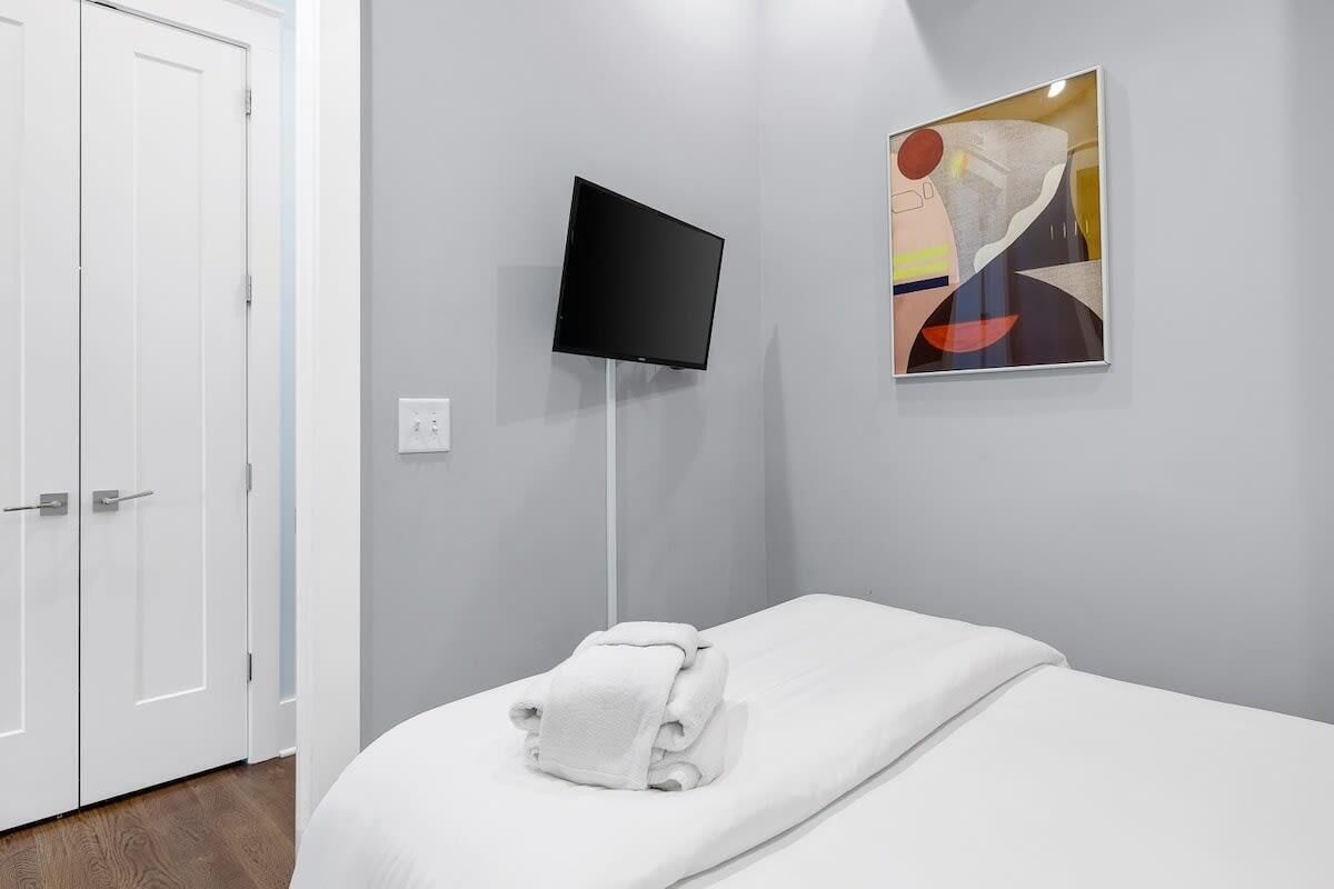 A hotel room with a bed, a television mounted on the wall, and a painting.