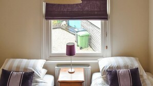 Un dormitorio con dos camas, una ventana con vistas al exterior, un radiador y una lámpara de mesa.