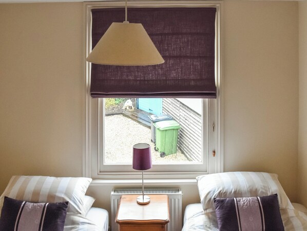 Un dormitorio con dos camas, una ventana con vistas al exterior, un radiador y una lámpara de mesa.