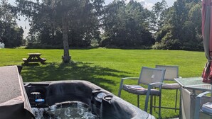 A hot tub with a table and chairs, a picnic table, and a grassy field with trees in the background. - Dog-Friendly large rural Estate just outside Alex Bay with hot tub and pool! (Alexandria Bay)