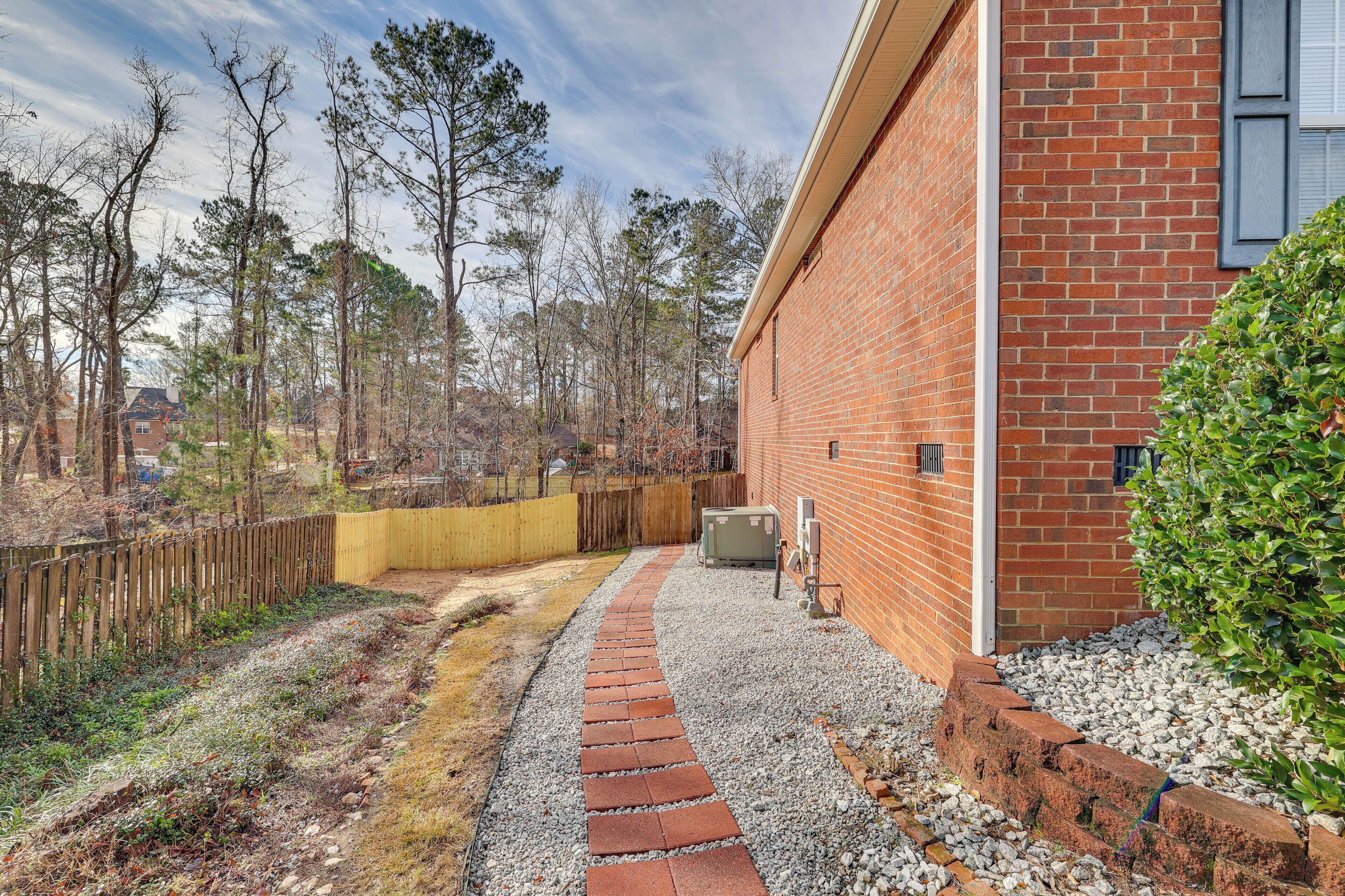 A brick building with a gravel pathway leading to a wooden fence.