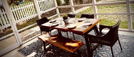 A patio with a wooden table set for four, surrounded by chairs, a bench, and a patterned rug.