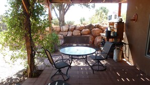 An outdoor patio with a round table and chairs, surrounded by a stone wall and greenery.