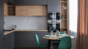 A modern kitchen with dark cabinetry, a wooden countertop, and a built-in oven. There is a dining table with chairs and a potted orchid on the windowsill.