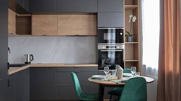 A modern kitchen with dark cabinetry, a wooden countertop, and a built-in oven. There is a dining table with chairs and a potted orchid on the windowsill.