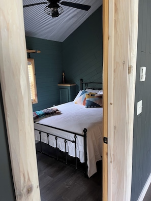Un dormitorio con cama, mesita de noche, ventana y ventilador de techo.
