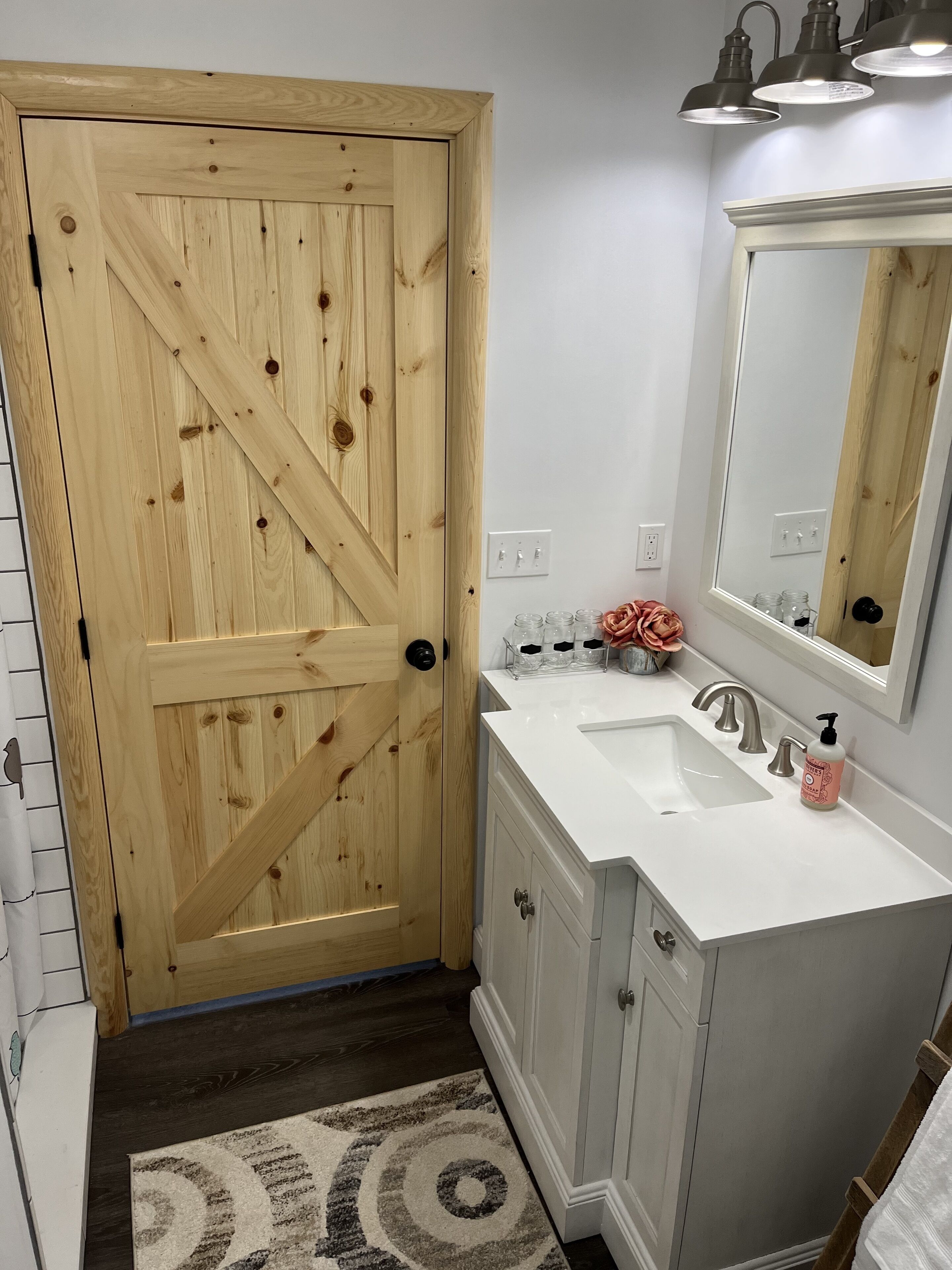 A bathroom with a wooden door, white sink, and a mirror.