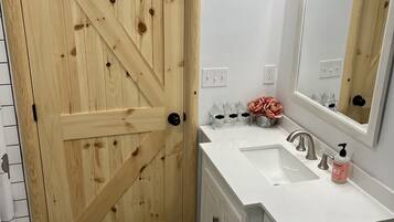 A bathroom with a wooden door, white sink, and a mirror.