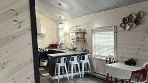 A modern kitchen with a central island, bar stools, and a dining table with chairs. - Super clean cabin near ORV trails & AuSable River, walking distance to town Mio. (Mio)