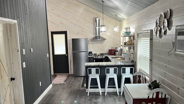 A modern kitchen with a central island, bar stools, and a dining table with chairs. - Super clean cabin near ORV trails & AuSable River, walking distance to town Mio. (Mio)