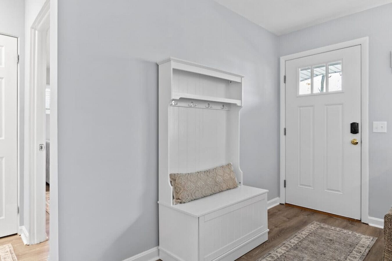 Un couloir avec un banc blanc, une porte et un tapis.