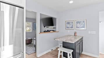 A compact kitchen with a built-in refrigerator, a small island with a white stool, and a flat-screen TV mounted above the island.