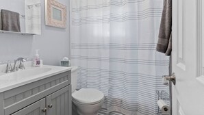 A bathroom with a white sink, a toilet, a shower curtain with horizontal stripes, and a towel hanging on the wall. - Lovely 2-Bedroom Condo, Close to Burlington/Airport! (South Burlington)
