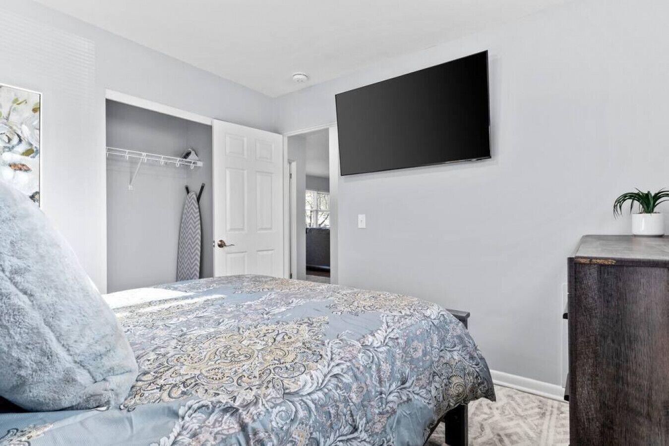 Quarto com cama, guarda-roupa, televisão de tela plana e planta em vaso.