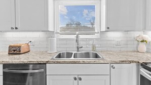 A kitchen with white cabinets, a stainless steel sink, a window with blinds, a toaster, and a vase with flowers. - Lovely 2-Bedroom Condo, Close to Burlington/Airport! (South Burlington)