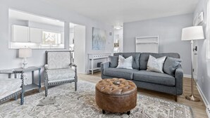 A modern living room with a grey sofa, a patterned rug, a wooden coffee table, and a leather ottoman. - Lovely 2-Bedroom Condo, Close to Burlington/Airport! (South Burlington)