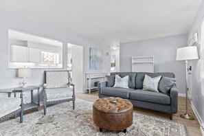 A modern living room with a grey sofa, a patterned rug, a wooden coffee table, and a leather ottoman. - Lovely 2-Bedroom Condo, Close to Burlington/Airport! (South Burlington)
