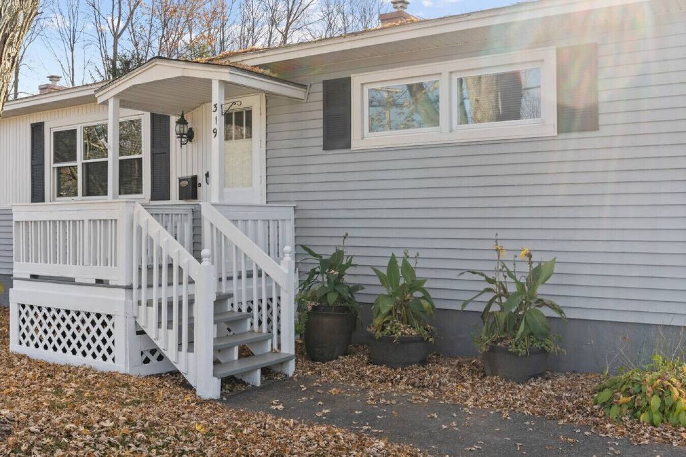 Einbungalow mit einer Veranda, einer kleinen angeschlossenen Garage und drei Blumentöpfen.