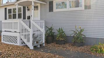 Einbungalow mit einer Veranda, einer kleinen angeschlossenen Garage und drei Blumentöpfen.