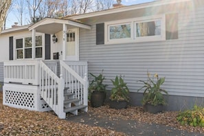 A single-story house with a front porch, a small attached garage, and three potted plants.