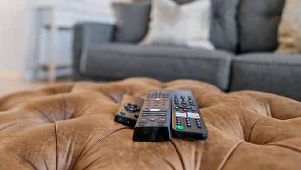 A brown tufted ottoman with three remote controls on it. - Lovely 2-Bedroom Condo, Close to Burlington/Airport! (South Burlington)