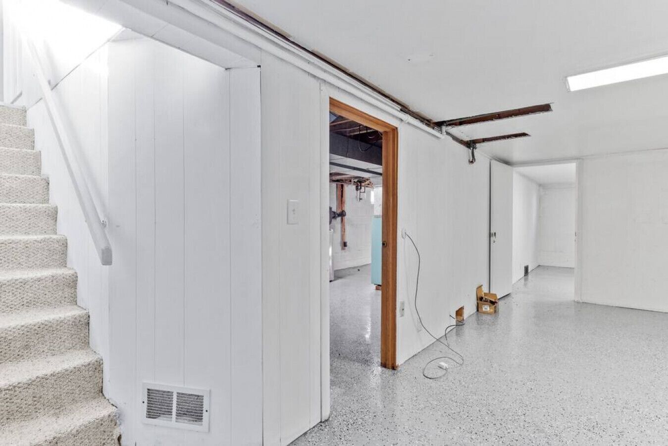 Interior espaçoso e moderno, com escada que leva a um segundo andar, um corredor com porta e uma área de serviços visível, com fiação aparente.