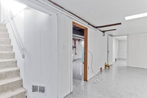 Un interior espacioso y moderno con una escalera que conduce a un segundo piso, un pasillo con una puerta y un área de servicios visible con cableado expuesto.