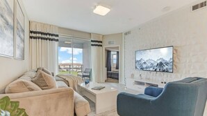 A modern living room with a sofa, a blue armchair, a coffee table, and a flat-screen TV mounted on a textured wall. - SUMMER SALE! Storey Lake 3BDRM (Kissimmee)