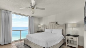 A bedroom with a large bed, a ceiling fan, two bedside tables with lamps, and a view of the ocean. - 🌅Amazing Floor to Ceiling Beach Views~Shoreline 2115 (Destin)