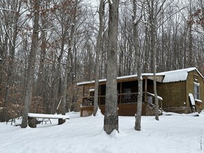 Eine Holzhütte mit Veranda und überdachtem Picknicktisch in einem verschneiten Wald.