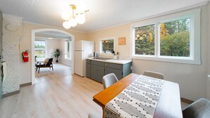 Eine moderne Küche mit einer zentralen Kochinsel, einem Essbereich mit Holztisch und großen Fenstern mit Blick auf Bäume.