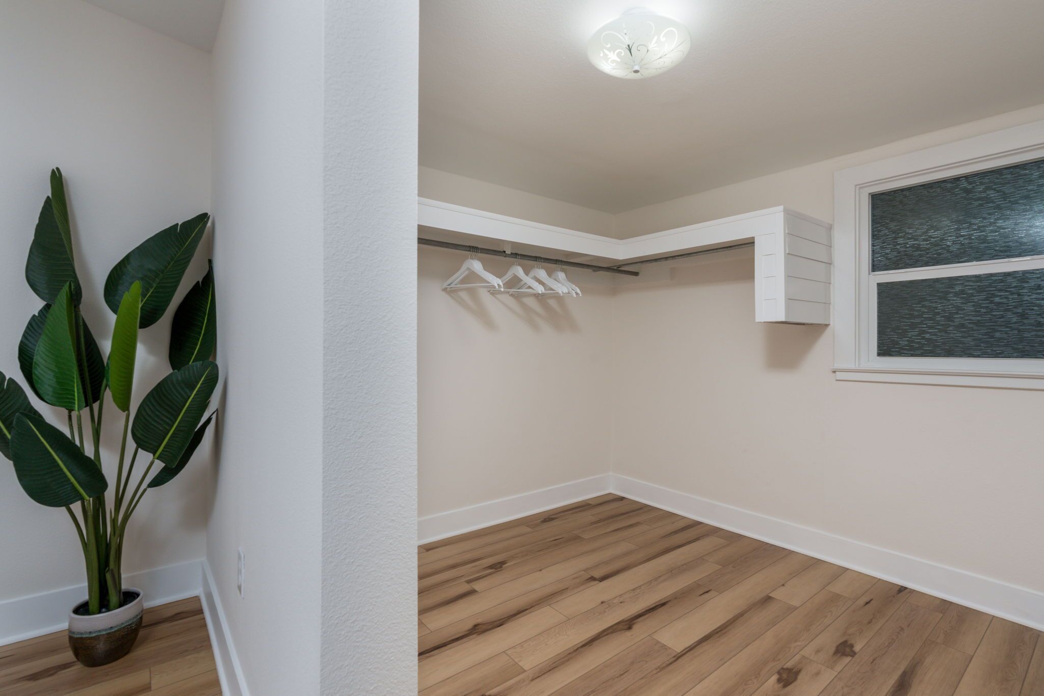 Ein Zimmer mit Holzboden, einer Topfpflanze, einer Deckenleuchte, einem weißen Wandgarderobe und einem Fenster mit Blick.