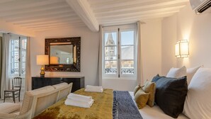 Habitación de hotel con cama, una silla, escritorio, espejo y ventana con vista a edificios.