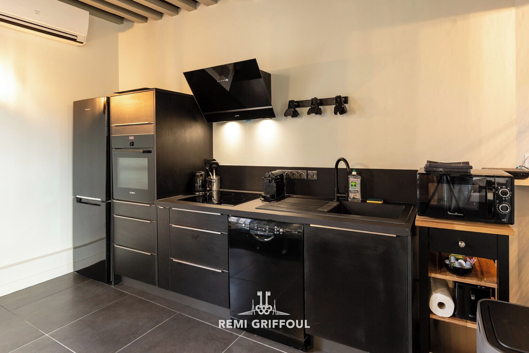 A modern kitchen with a stainless steel refrigerator, built-in oven, and dishwasher. There is a microwave on a wooden shelf, and a coffee maker on the counter.