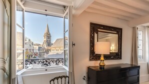 Una habitación con un amplio ventanal con vistas a un pueblo histórico, un aparador negro y un espejo con lámpara.