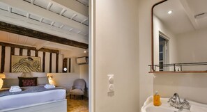 Quarto de hotel com cama, cadeira, espelho grande e pia.