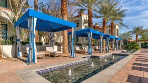 A poolside area with blue canopies, lounge chairs, and a water feature.