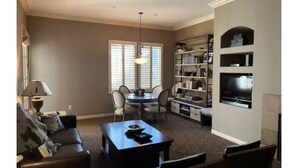A living room with a sofa, a coffee table, a dining table with chairs, a TV, and a bookshelf.