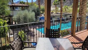 A pool area with a view of mountains, palm trees, and a covered patio with a table and chairs.